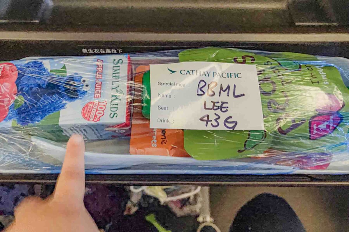 Airplane tray with packaged baby meal and snacks labeled “CATHAY PACIFIC Special meal BBML LEE 43G” with juice and baby pouches, showing how you might feed a baby on a flight.