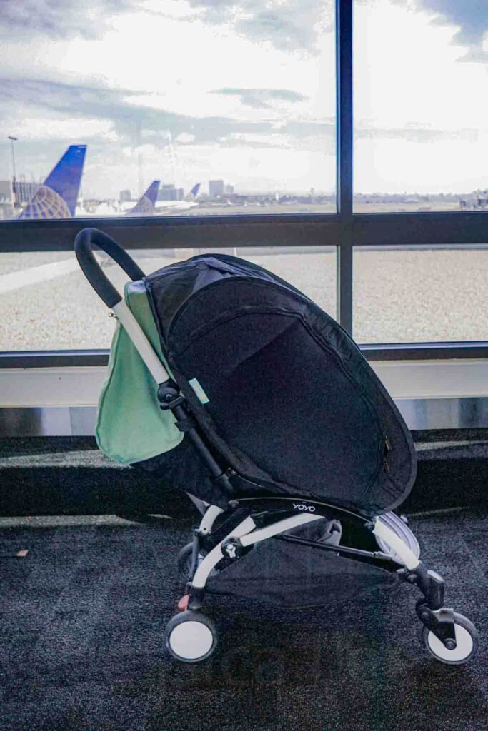 Babyzen yoyo travel stroller with a black Cozigo blackout cover fully enclosing the seat near airport windows. This baby blackout solution helps baby nap on the go and improves baby sleep while traveling by blocking light and distractions.