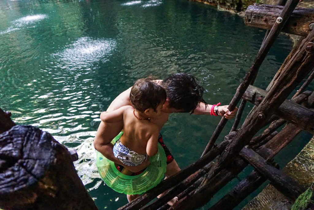 Dad carrying toddler down ladder into cenote pool