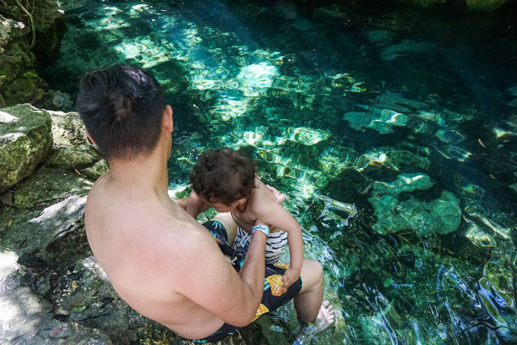 Dad holding toddler over Cenote Azul pool rocks