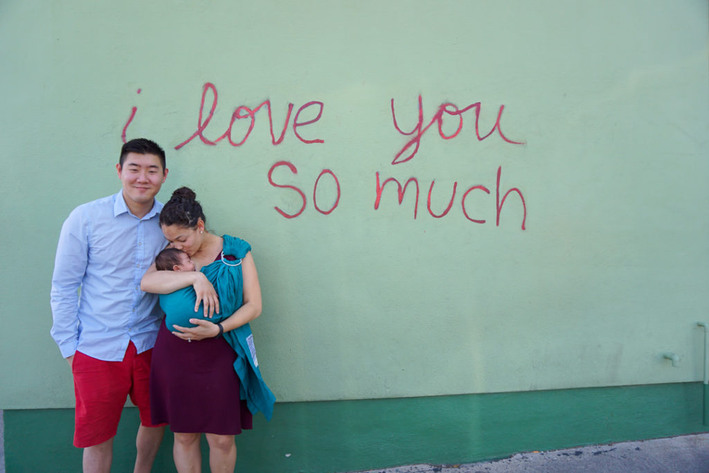 Young mixed family mom kissing newborn baby in front of I love you so much mural on South Congress Street in Austin