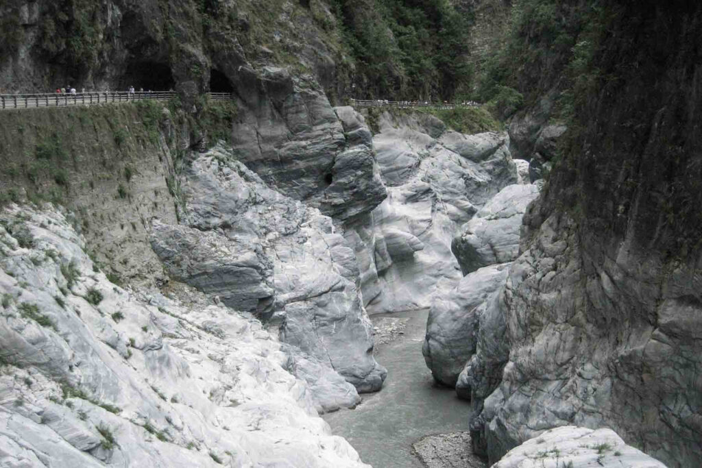 Towering marble cliffs enclose a winding river deep in Taroko Gorge National Park, Taiwan. The stone has dramatic layers of gray and white, carved by centuries of flowing water.
