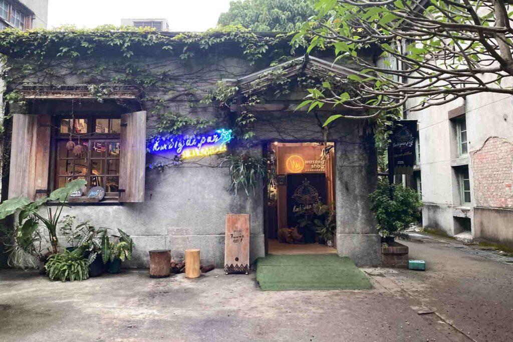 Ivy-covered gray concrete building with rustic wood window shutters and neon signs, including "wasang show" and glowing script above the entrance, located at Huashan 1914 Creative Park in Taipei.