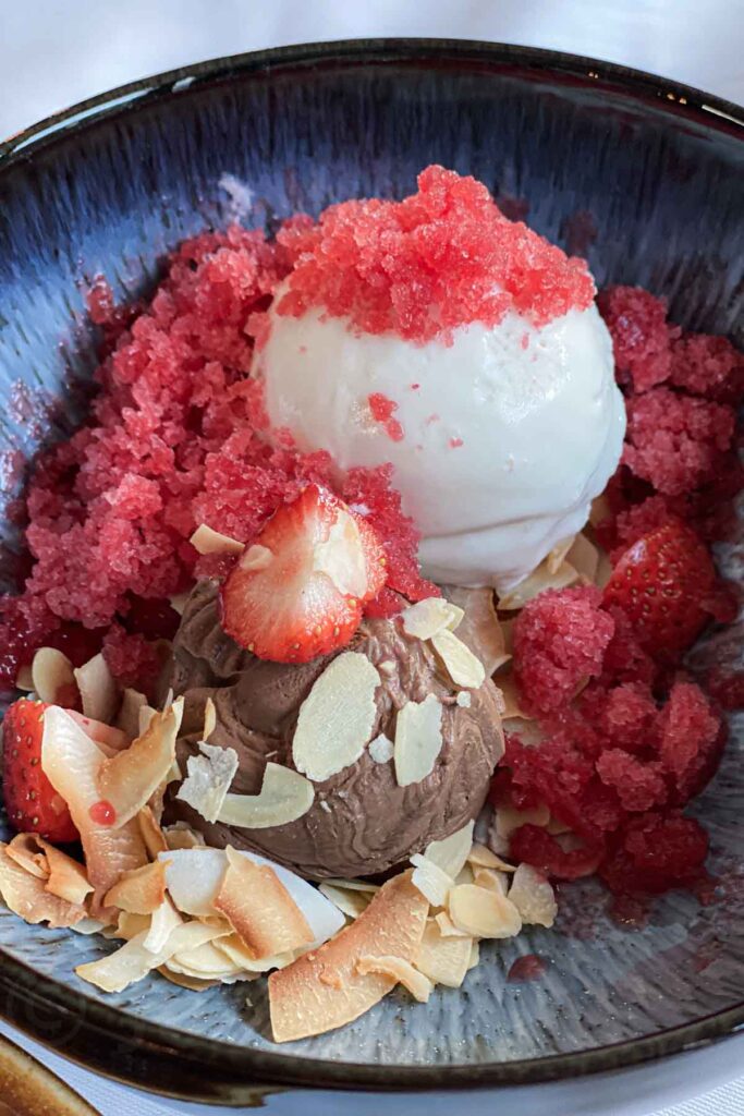 Close-up of a dessert bowl with scoops of white and chocolate ice cream topped with red granita, fresh strawberries, and toasted coconut flakes served at the Lava Restaurant at the Blue Lagoon.