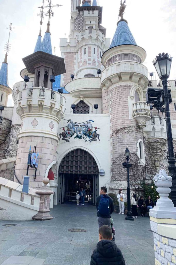 A child and adult approach a grand castle entrance with blue spires and medieval-style murals, at Lotte World Adventure amusement park in Seoul, Korea.