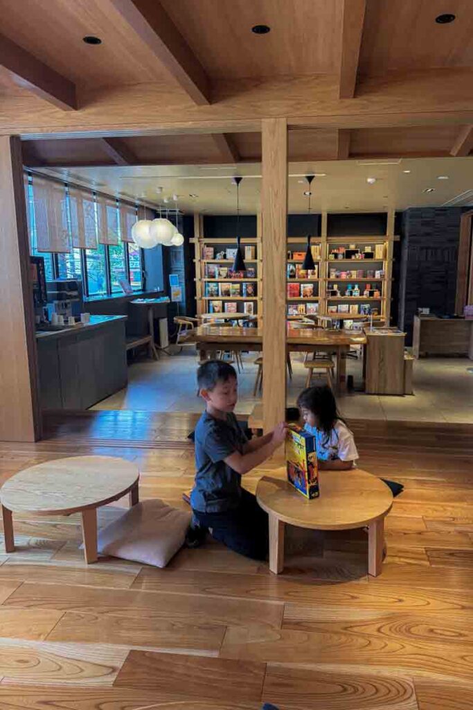 A young boy and toddler girl sit at low wooden tables in the hotel’s board‑game lounge, digging into a new game together during their stay.