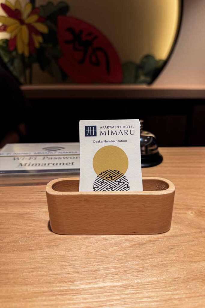 A close‑up of a stack of the business cards displayed at the front desk of the hotel in Osaka, set in a wooden holder with elegant Japanese‑style décor.