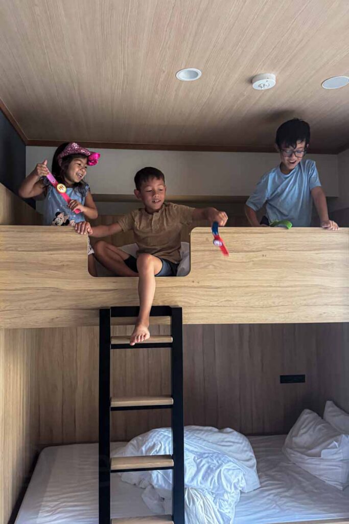Happy children climb and play on the top bunk in a family apartment at the Mimaru Osaka Namba hotel in Japan, highlighting the fun sleeping arrangement.