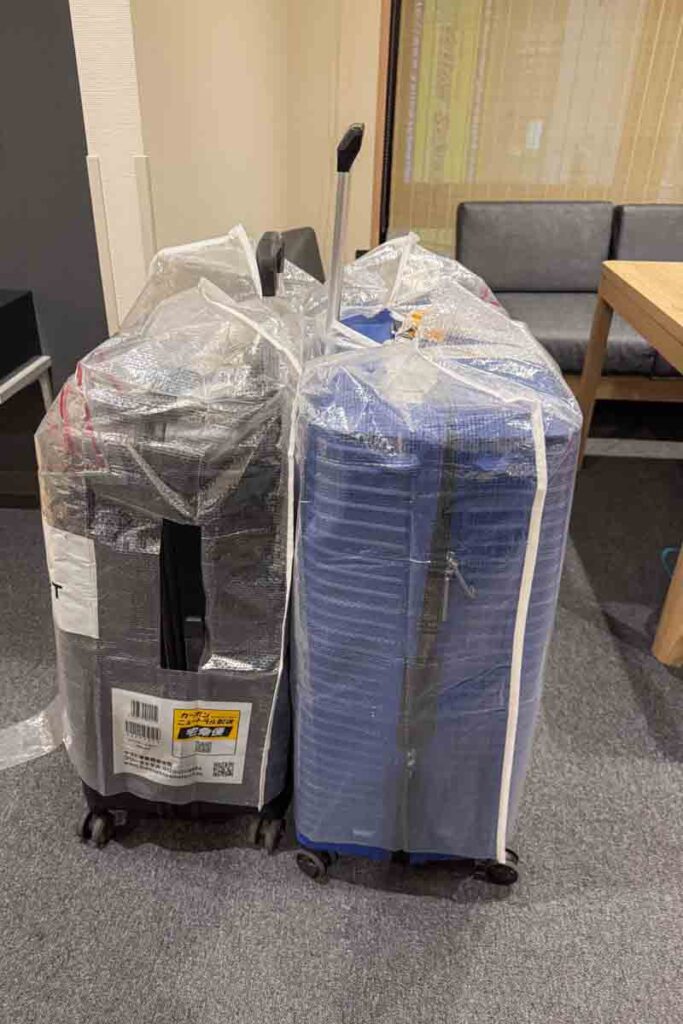 Two large suitcases are wrapped in plastic covers and labeled, waiting in a hotel room after being delivered to the family’s hotel in Osaka. This shows how convenient and secure the suitcase delivery service in Japan can be for tourists.
