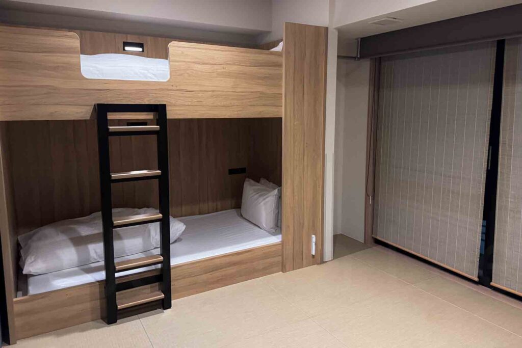 A family apartment room at Mimaru Osaka Namba Station with built‑in wooden bunk beds, tatami floor with space for futon sleeping, and a large window covered by blinds — designed for families.