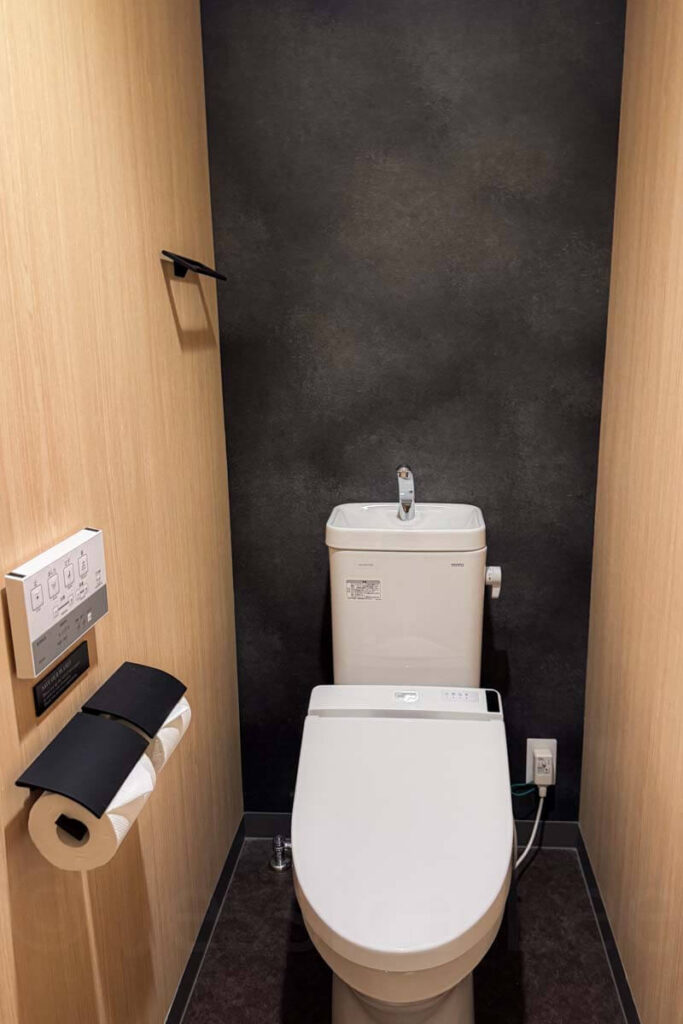 Minimalist toilet room with wood paneling and black accent wall in the hotel apartment, the toilet is the typical smart Japanese Toto bidet style.