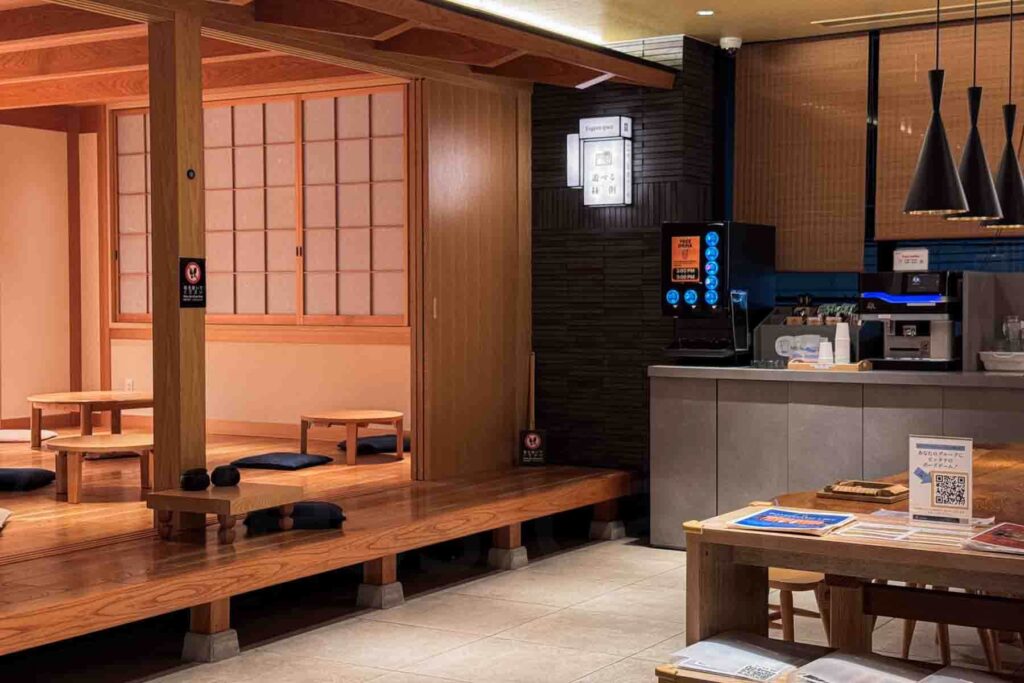 A communal lounge in Japanese style with wooden tables, self serve drinks, and a tatami‑style board game play zone — a comfortable spot for families at the hotel.