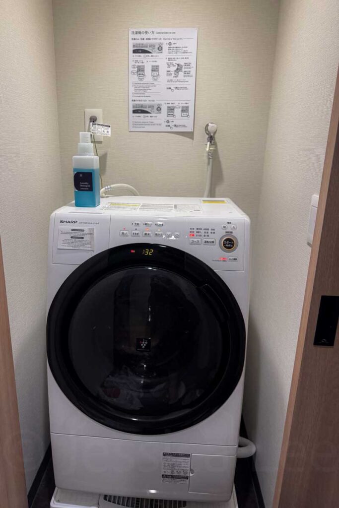 An in‑apartment Sharp brand front loading white washer/dryer combo in the family apartment at Mimaru Osaka Namba.
