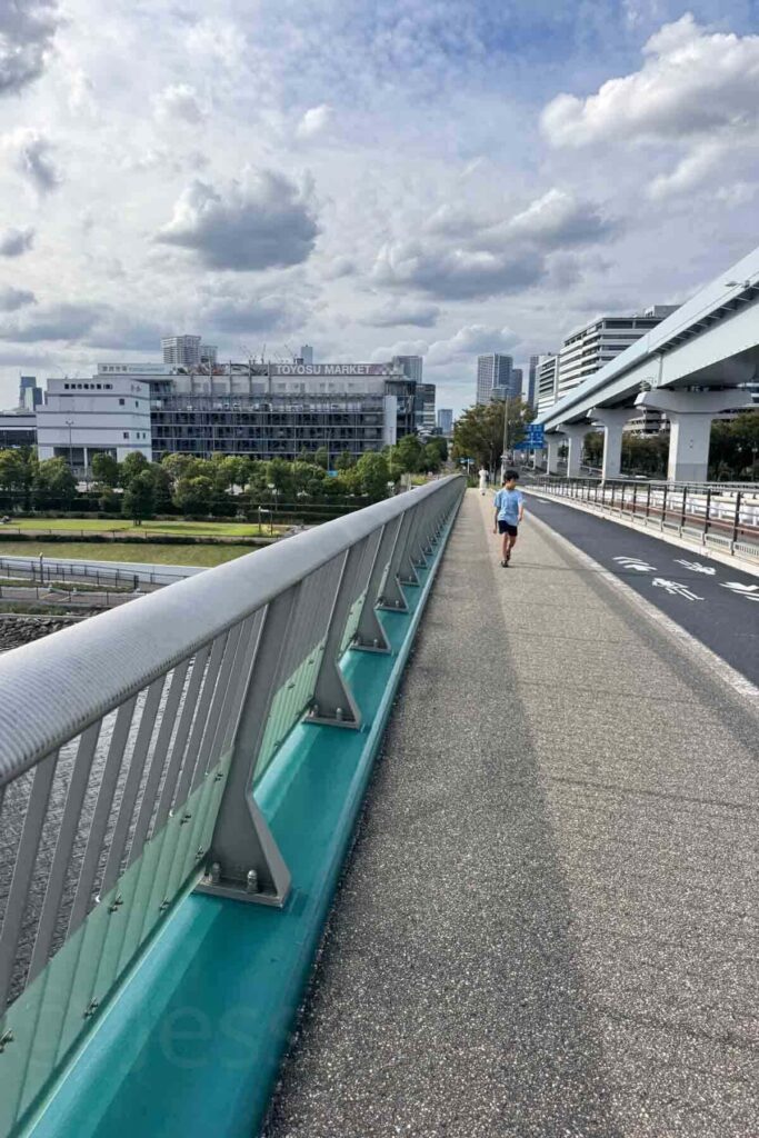 A child walks along the Toyosu Market pedestrian bridge under a cloudy but bright sky in tokyo in September.