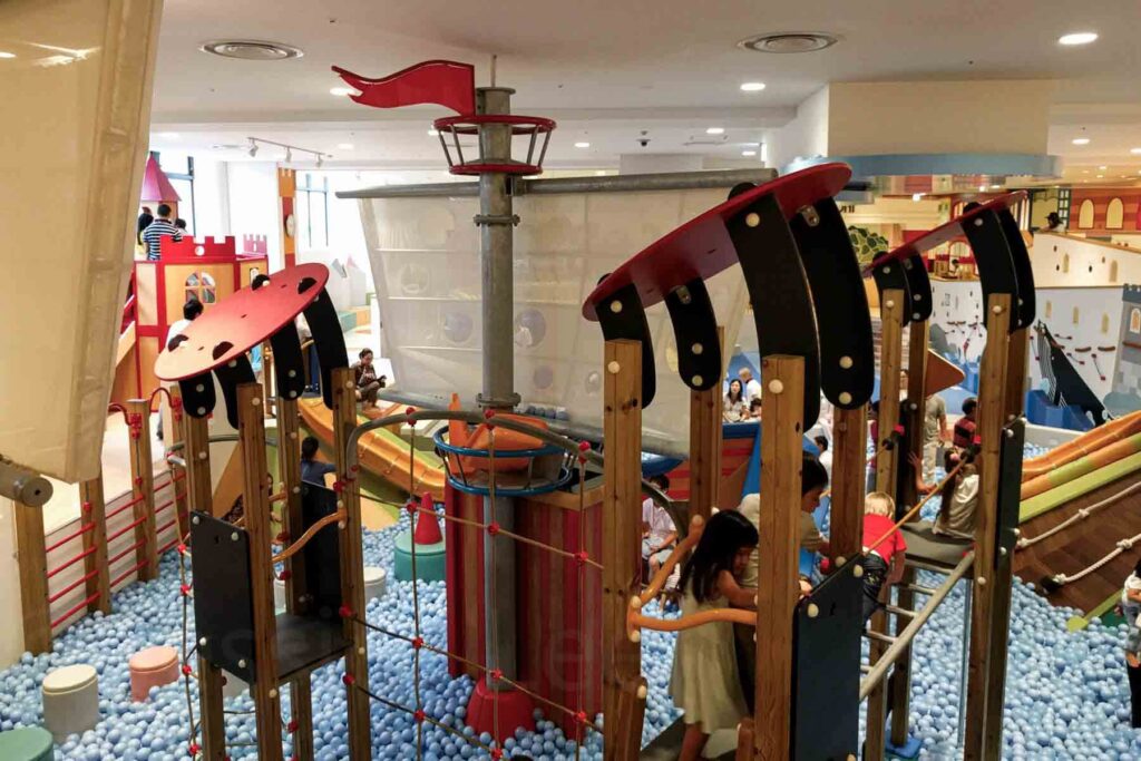 Children climb and play on a pirate ship-themed indoor playground. Below the “water” is a blue ball pit. This colorful and energetic space is a top pick indoor kids attractions in Tokyo.