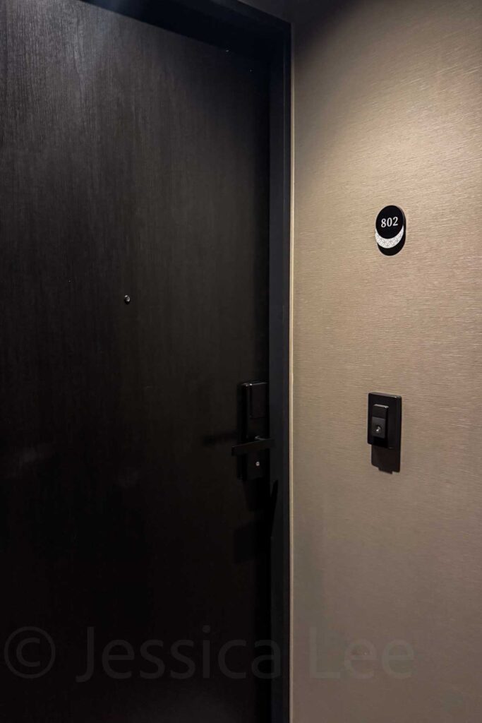 Close-up of a dark black wooden hotel room door marked 802 with a keycard reader outside. Entry to a Mimaru Suites Tokyo Asakusa hotel family room.