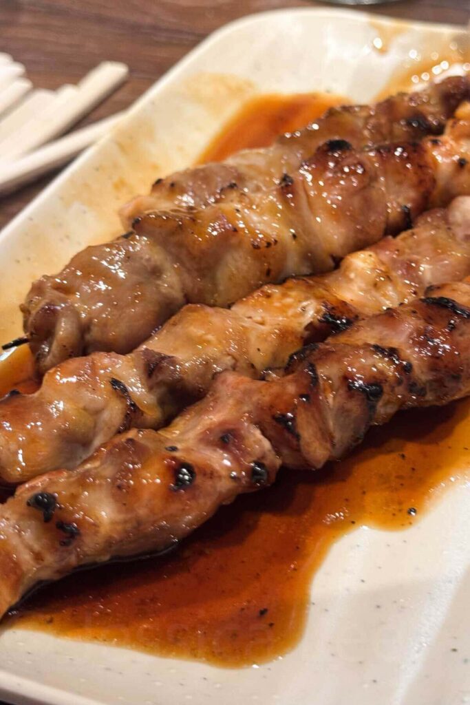 Close-up of juicy grilled chicken yakitori skewers glazed in a savory sauce, served on a white plate.