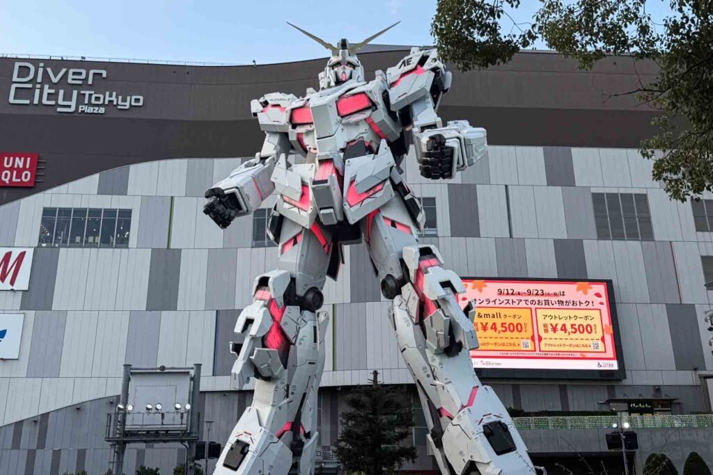 A towering white Gundam robot statue glows red outside DiverCity Tokyo Plaza.