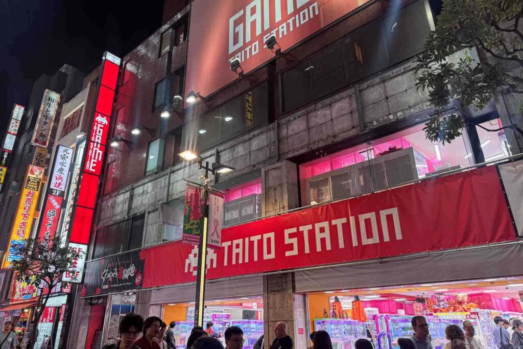 The exterior of Taito Station arcade in Shinjuku, Tokyo glows with a bold red sign as people gather around the entrance. A lively and colorful gaming center that's one of the most fun things to do in Tokyo for kids who love claw machines and retro games.