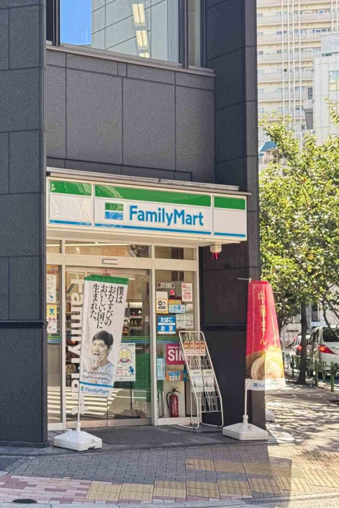 A small FamilyMart convenience store in Tokyo with bright signage and banners outside on a sunny day.