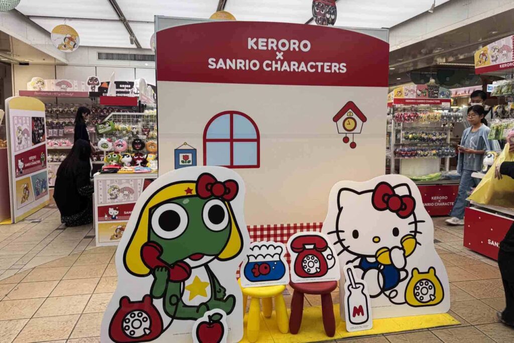 A Keroro x Sanrio Characters display featuring cartoon cutouts of Hello Kitty and Keroro next to themed merchandise along Character Street in Tokyo Station.