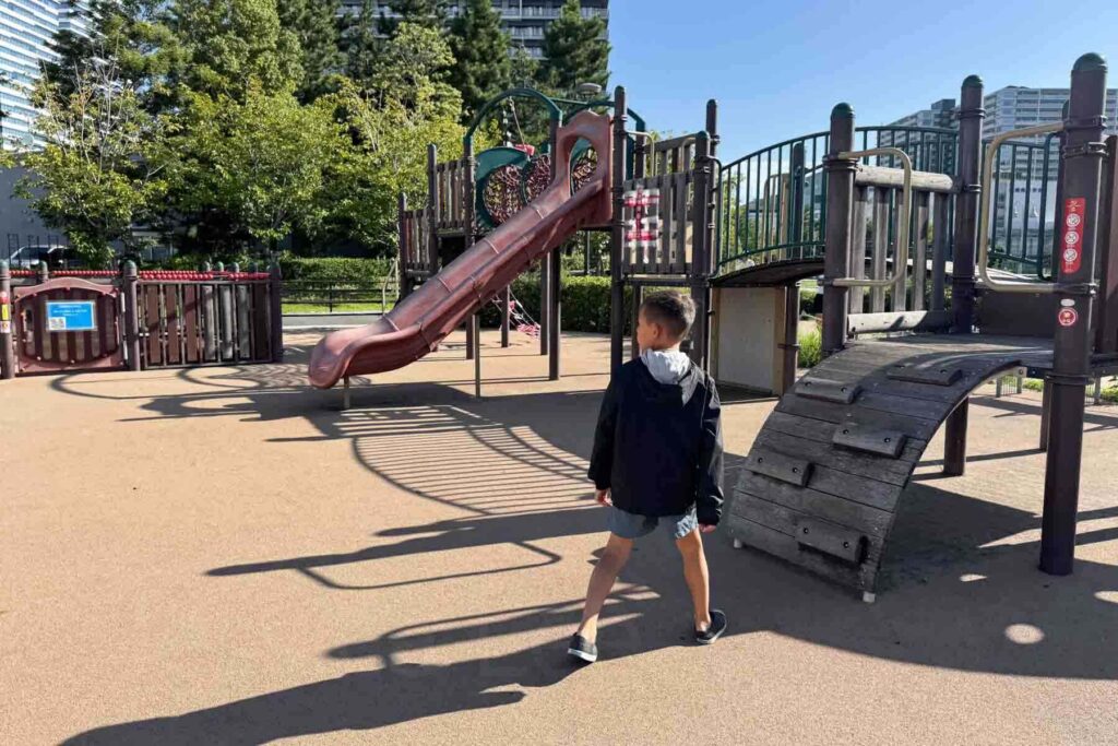 A child walks through a typical playground structure with slides and climbing structures surrounded by greenery in Tokyo. Free outdoor playgrounds are a great option for free things to do in Tokyo with kids.