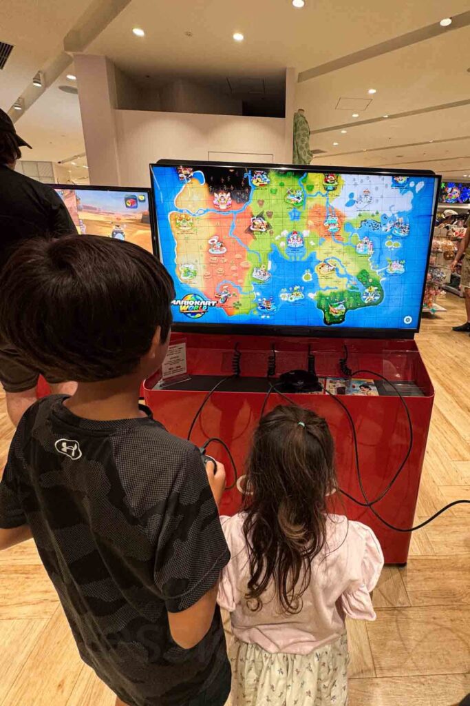 Two children play Mario Kart at the Nintendo Store in Shibuya Parco, their eyes focused on the colorful game map on screen. This shopping mall in Tokyo offers fun things for kids to do, not only shopping.