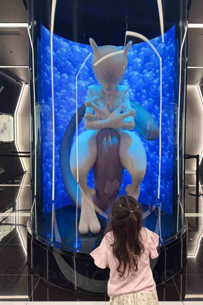A young girl stands in awe before a giant illuminated Mewtwo display in a tank at the Pokémon Center in Tokyo.