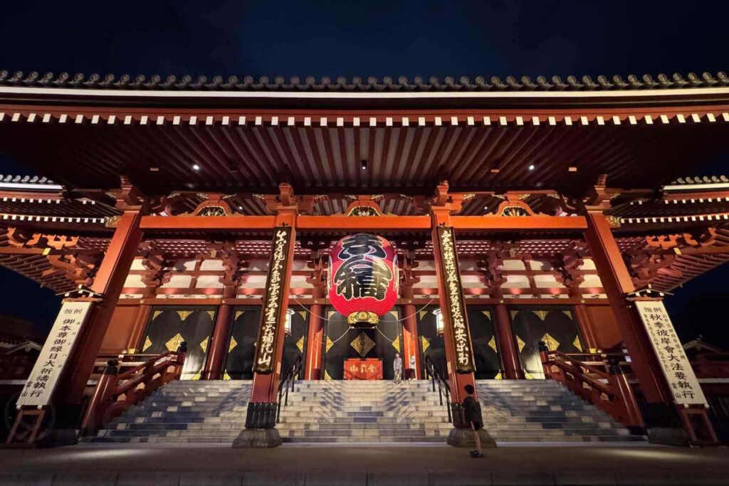 The main hall of Senso-ji Temple glows warmly under night lighting, with its grand red lantern and wide stone steps. Kids walk up the steps during an uncrowded moment.