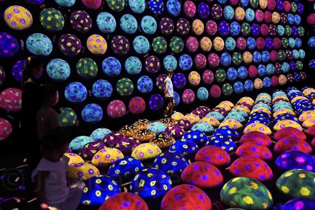 Children explore a dark glowing room filled with hundreds of multicolored, egg-shaped lights in the TeamLab Planets Tokyo art installation. This immersive digital museum is one of the top kids attractions in Tokyo.