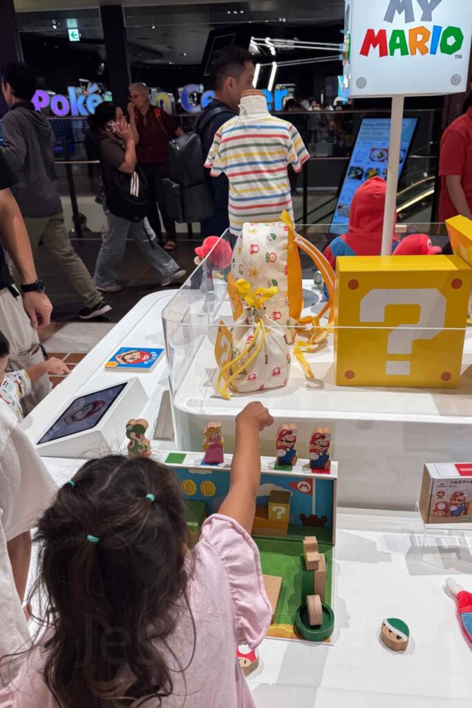 A young child plays with Mario-themed wooden toys at the Nintendo Store in the Parco Shibuya shopping mall in Tokyo, surrounded by interactive displays and merchandise.