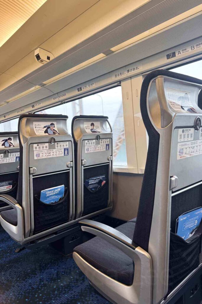 Inside view of a Keisei Skyliner train in Tokyo traveling from Narita airport to the city with sleek gray and black seats, tray tables, and window views. Riding these high-speed trains is a smooth and comfortable way to get around when visiting Tokyo with kids.