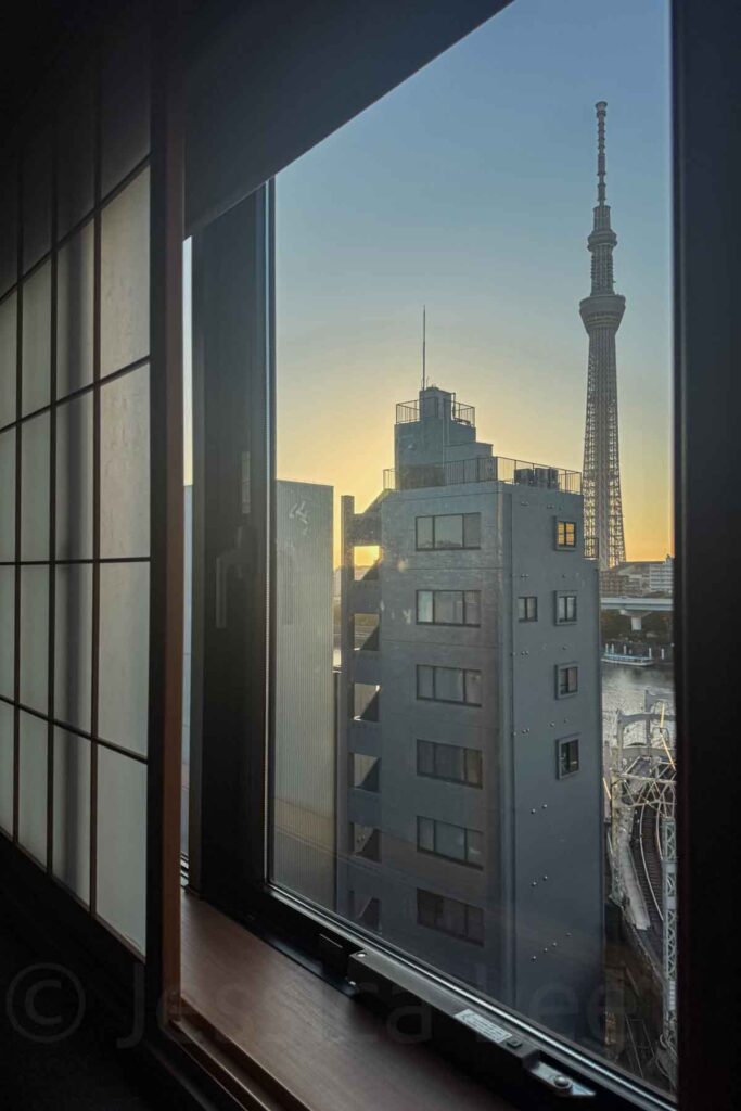 View of Tokyo Skytree and nearby buildings at sunrise seen through a hotel window with shoji-style panels. Great view from room 802 at Mimaru Suites Tokyo Asakusa.