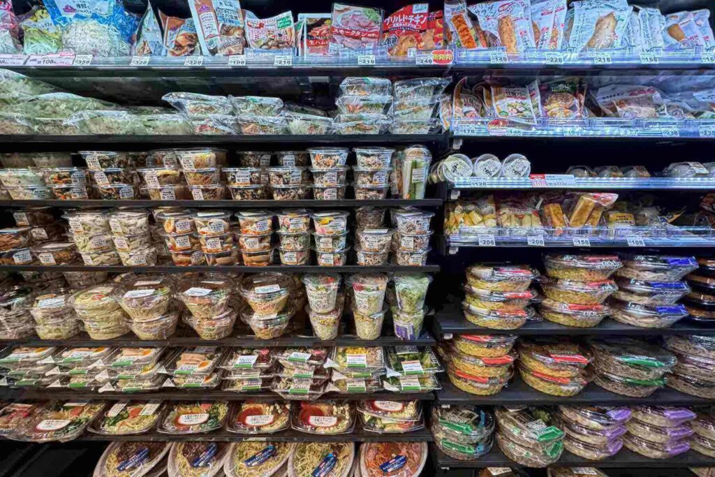 Shelves at a Japanese convenience store, Ministop, are filled with neatly arranged salads, noodles, and packaged meals.