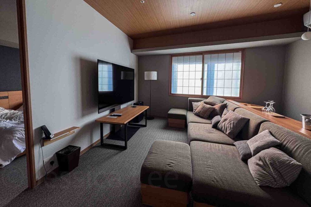 Modern Japanese two-bedroom hotel suite at Mimaru Suites Tokyo Asakusa living area with a large sectional, TV, and adjoining bedroom. Spacious layout perfect for families looking for the best places to stay in Tokyo with kids.