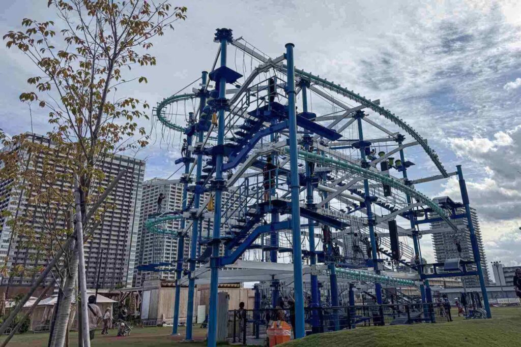 A towering blue and white multi-level rope course structure at Toyosu, with kids climbing and navigating suspended obstacles located at livedoor Urban Sports Park in Tokyo.