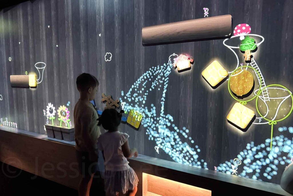Two kids interact with a projection wall in a dark room at TeamLab Tokyo, moving pieces and activating animations with glowing effects. A family friendly Tokyo attraction perfect for curious, creative kids.