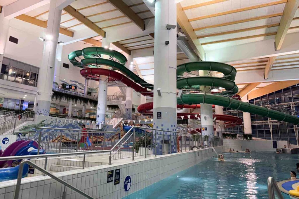 A spacious indoor waterpark with large red and green waterslides and a swimming pool, offering warm fun for families during a winter getaway to Zakopane, Poland.