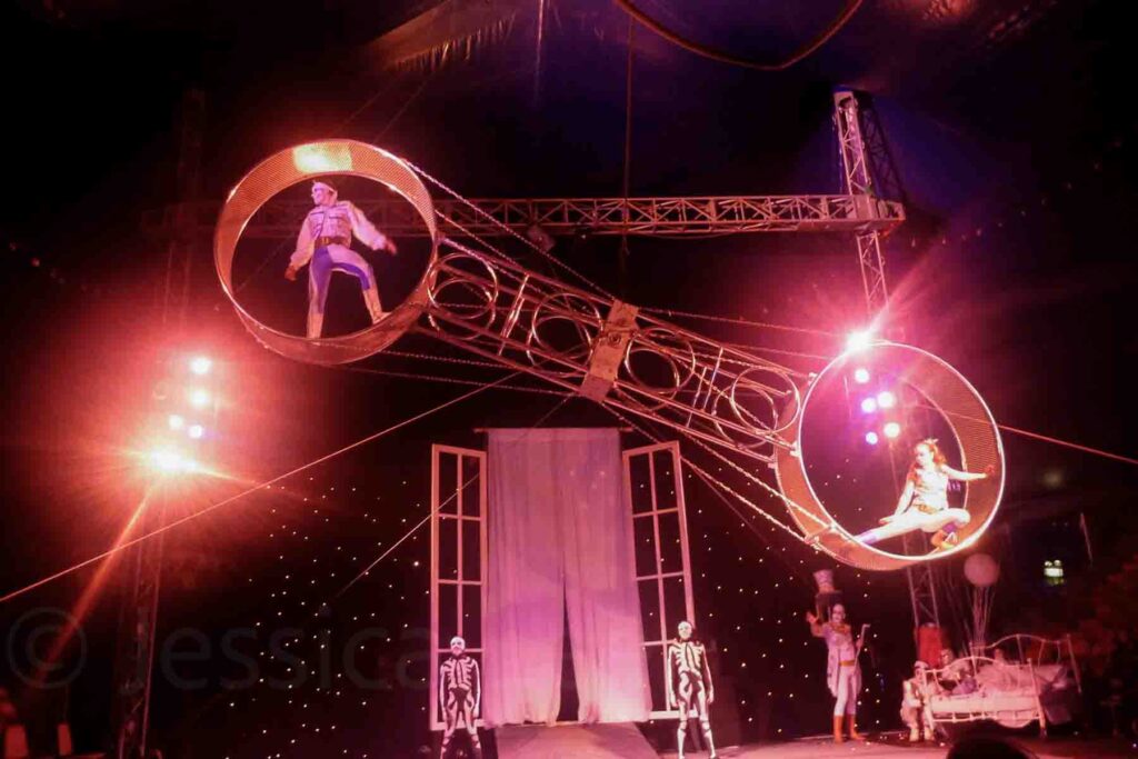 Acrobats perform a daring stunt inside spinning metal wheels suspended high above a circus stage lit with pink and red lights at Winter Wonderland in Hyde Park, London.