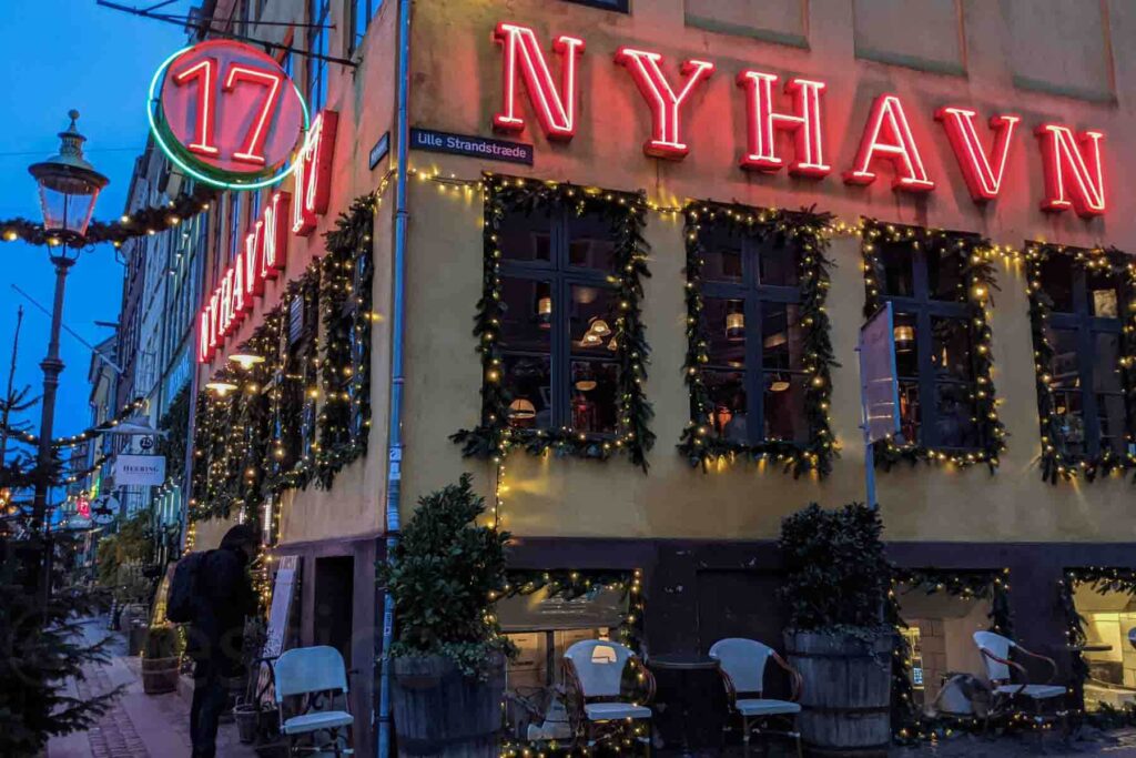 The iconic Nyhavn 17 restaurant in Copenhagen glows under festive garlands and lights, with holiday decor twinkling against the dark blue evening sky. A picture‑perfect stop during a holiday trip.