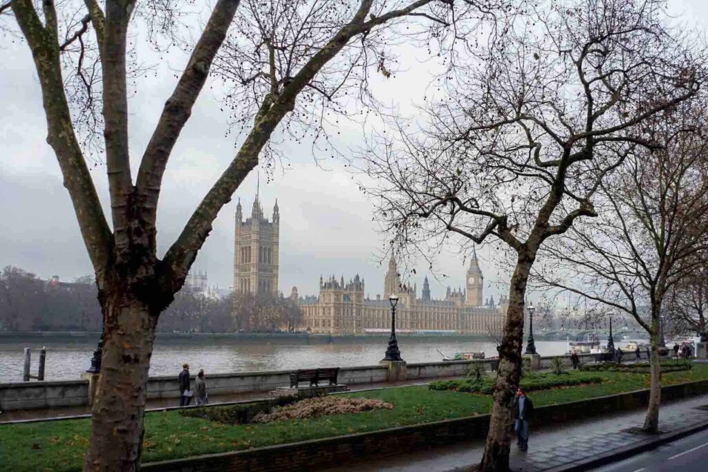 A wintry view of the Palace of Westminster and Big Ben seen from across the River Thames, framed by bare trees during December in London.