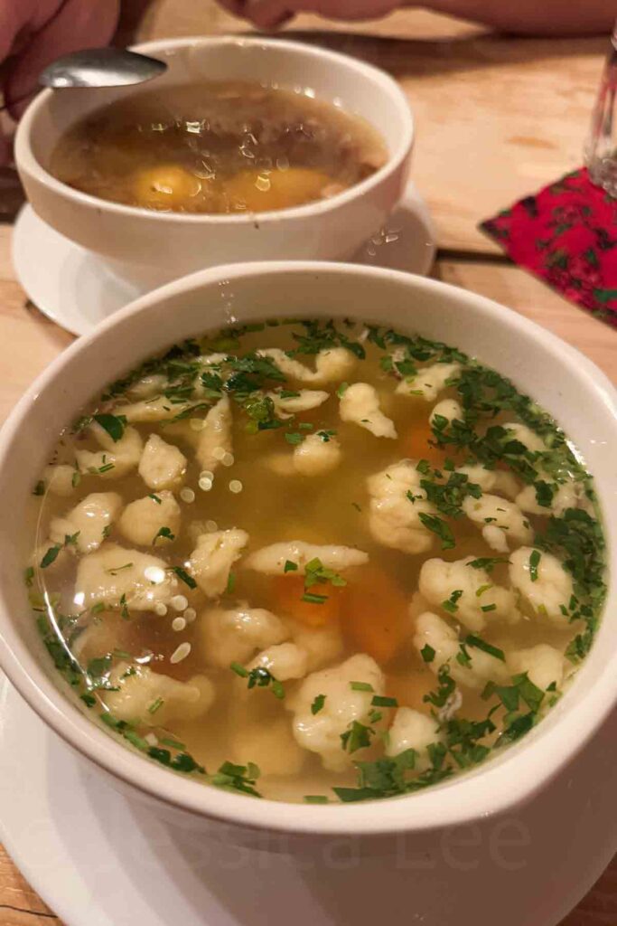 Two bowls of hearty Polish‑style soup served on a wooden table in white bowls, one with dumplings in a clear chicken broth and the other with rich stew. A comforting winter meal during a cozy Christmas destination getaway in Zakopane.