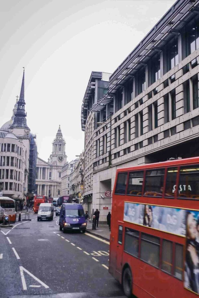 A red double‑decker bus drives past St. Paul’s Cathedral on a cloudy winter day in London, surrounded by historic buildings.