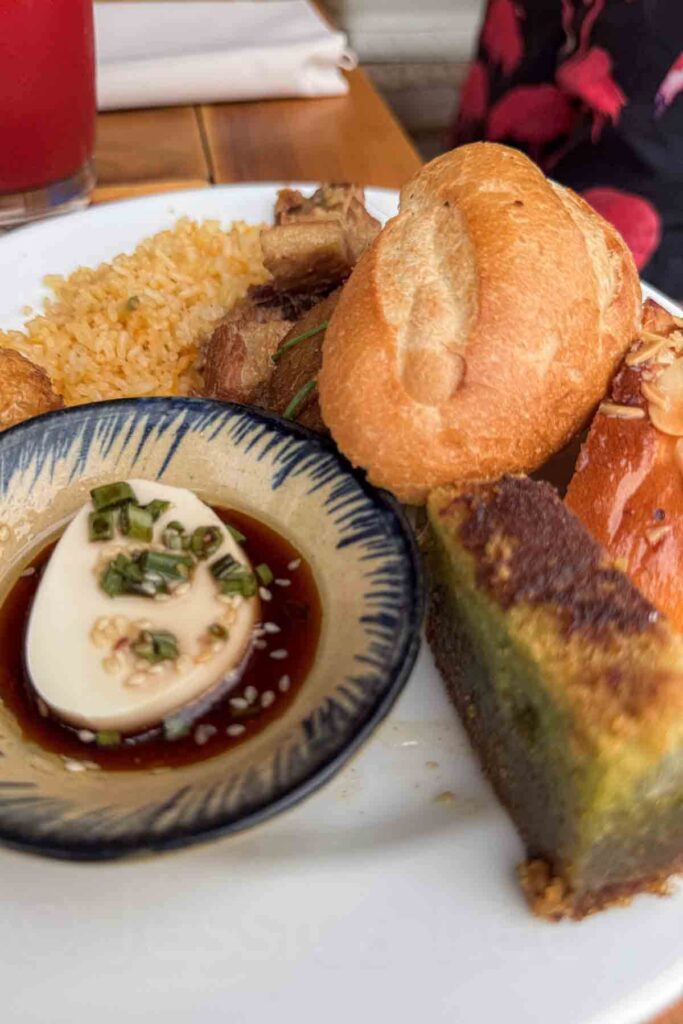 Plate with a variety of breakfast items including tofu in soy sauce, bread rolls, rice, braised meat, and a slice of green pandan loaf from the breakfast buffet at Hyatt Regency Danang.