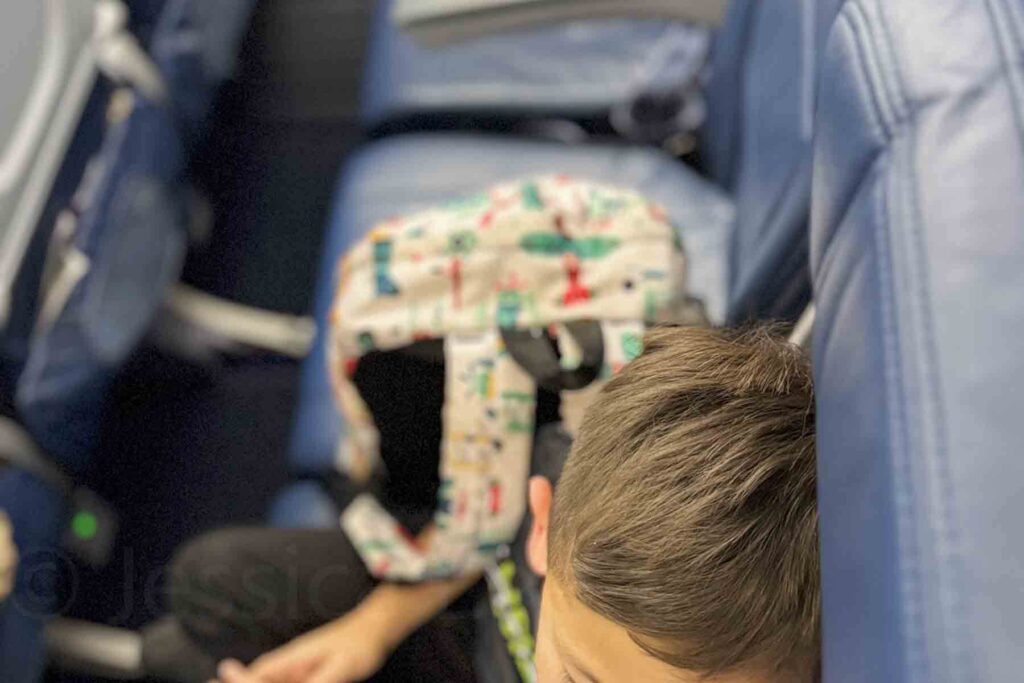 Up close overhead shot of a child relaxing on an airplane seat with a travel-themed backpack beside him on the blue seats.
