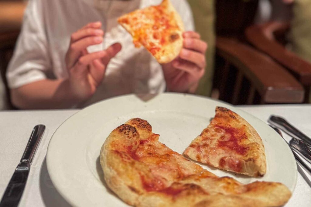 Close-up of a child eating a slice of a personal cheese pizza at the Italian restaurant at Hyatt Danang Resort, with three more slices on a white plate.