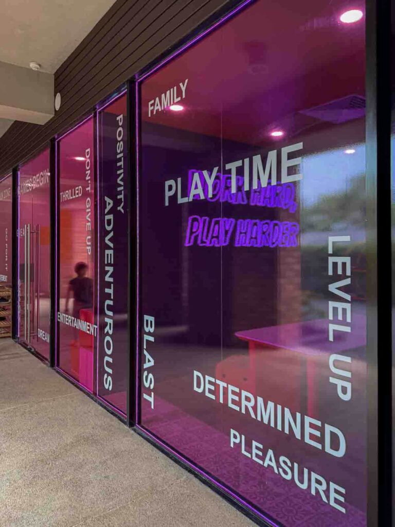 Wall of the big kids' play room and arcard at Hyatt Regency Da Nang with neon signage and motivational words like “Play Time,” “Level Up,” and “Family.”