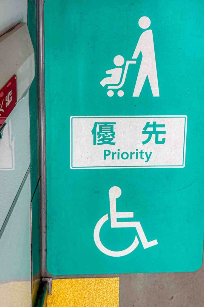 Green aqua priority seating sign in Japan showing a parent with a stroller and a wheelchair symbol with the text Priority in English and Japanese. Helpful example of accessible public transport.