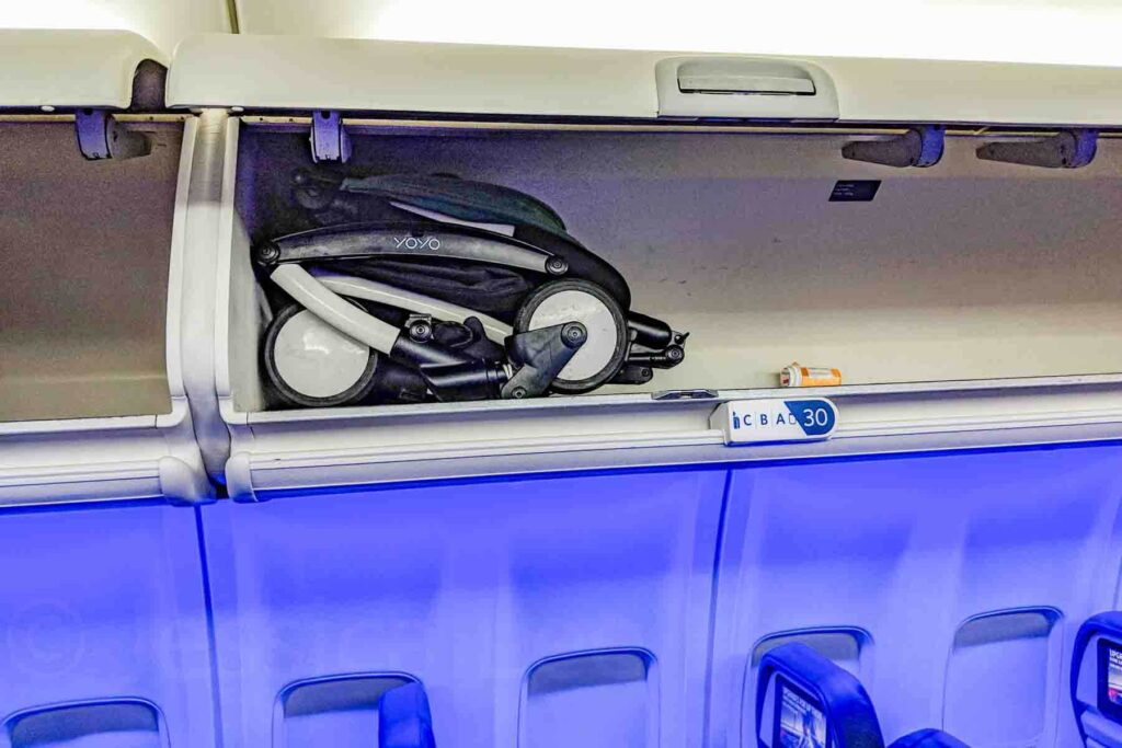 Babyzen Yoyo+ stroller folded and stored in an airplane overhead bin on a Delta airplane, demonstrating how easily it fits and why it is considered one of the best travel stroller options for flying with a baby.