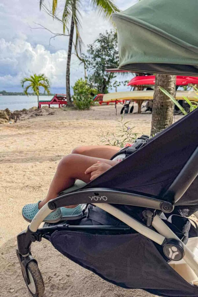 Toddler relaxing in a green Babyzen Yoyo travel stroller on the beach in Bocas del Toro, Panama.